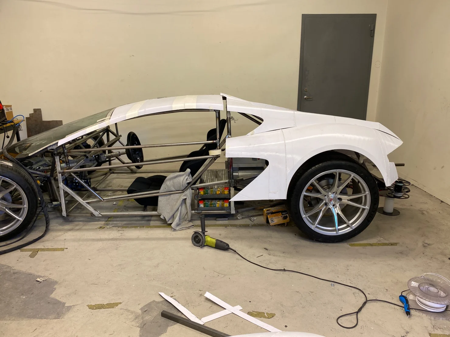 Electric supercar under construction with white bodywork trial-fitted around its exposed tubular chassis