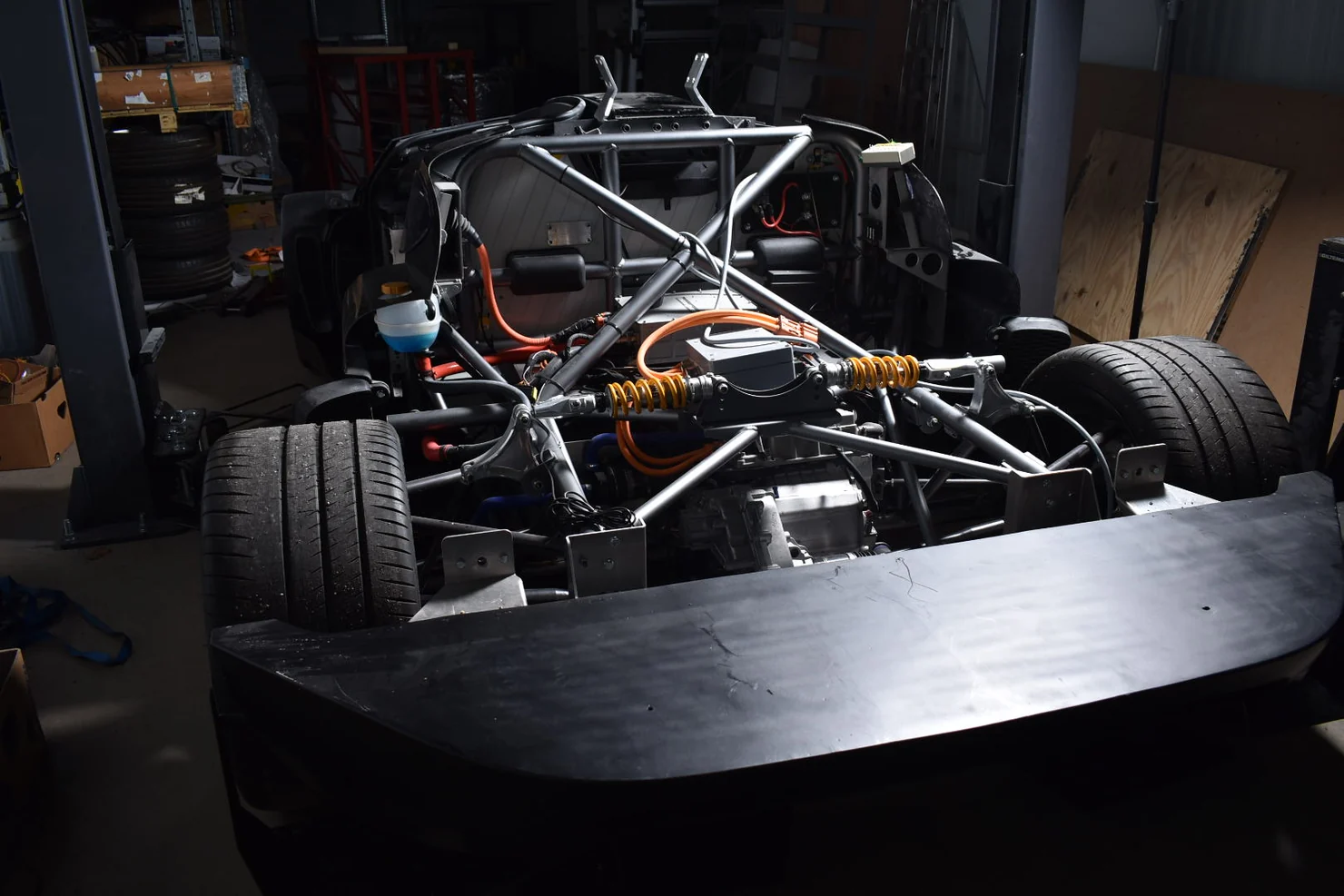 Exposed rear systems of a tubular chassis with suspension, orange cables and large tires in a working workshop